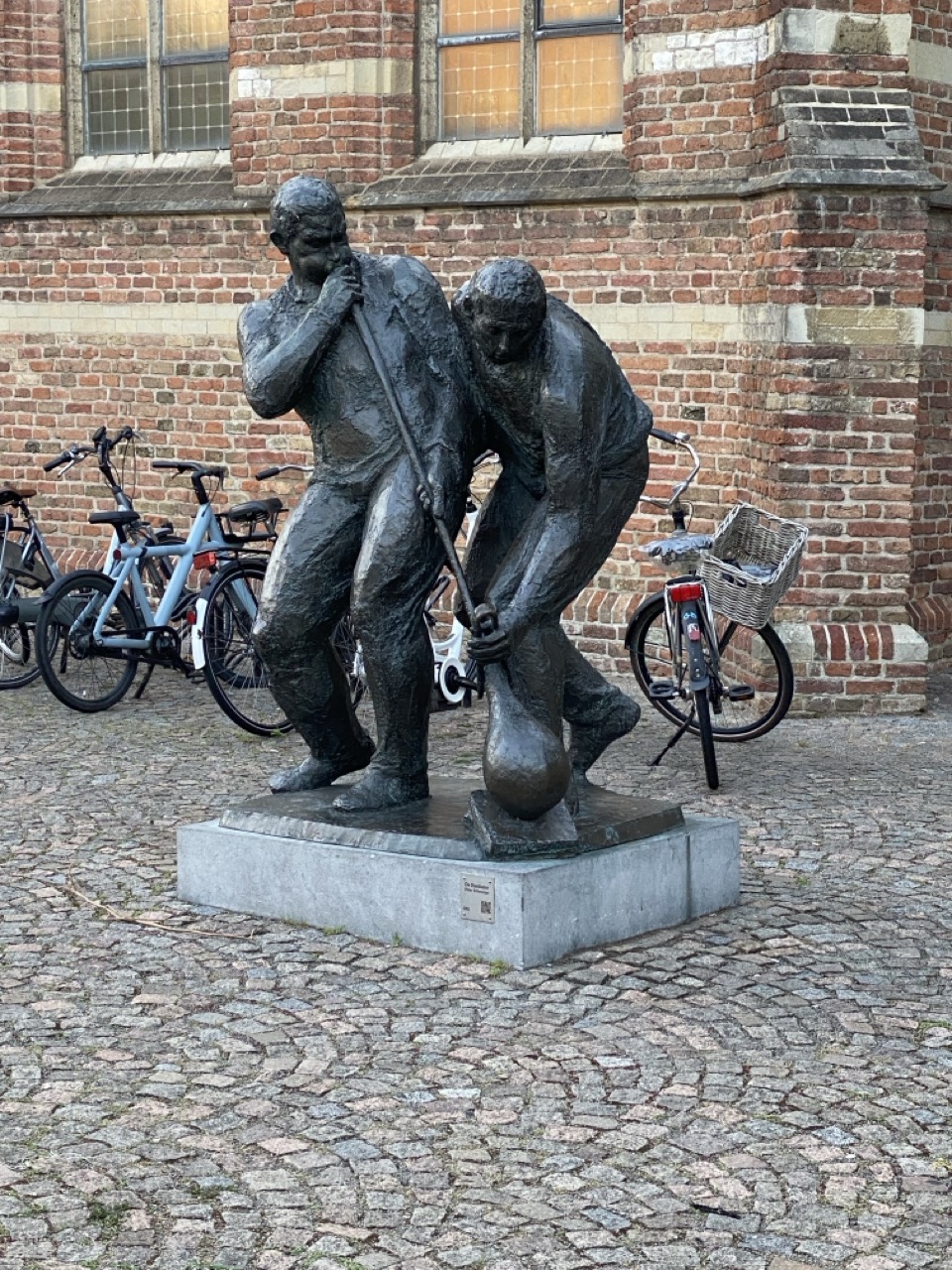 Een groot beeld van een man die glas blaast en zijn assistent die met een tang het glas vasthoud. 